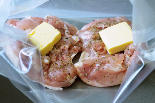 Vacuum sealed chicken thighs with a pat of butter preparing for sous vide.