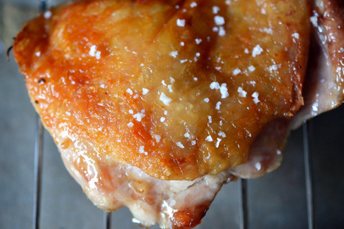 A sous vide crispy chicken thigh resting on a cooling rack with fleur de sel on the skin.