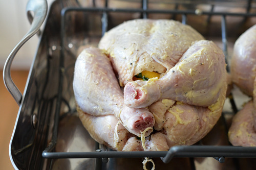 A raw chicken trussed and covered with butter on a roasting rack.