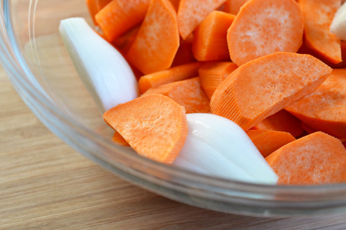 A closeup of a bowl filled with a bowl,chopped carrots, yams, and onions.