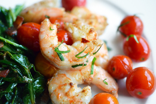 Tabil seasoned shrimp on a plate with sautéed spinach and cherry tomatoes.