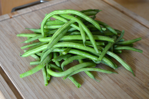 A pile of green beans on a wooden cutting board. 
