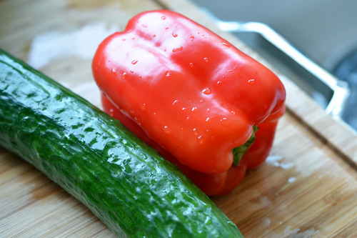 A red bell pepper and cucumber on a cutting board.
