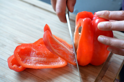 Someone cutting a red bell pepper.
