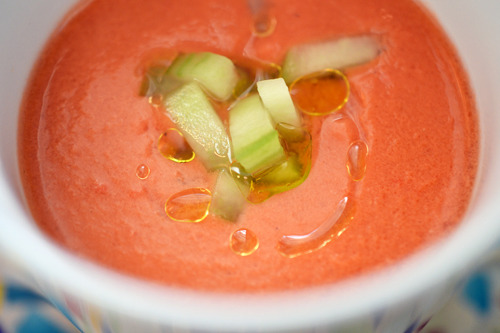 A bowl of watermelon and tomato gazpacho topped with olive oil and cucumber.