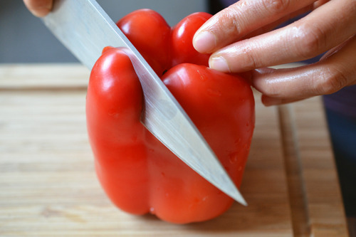 Someone cutting a red bell pepper.
