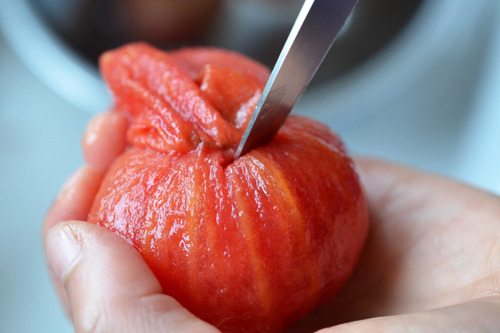 Someone coring a boiled tomato with a knife.