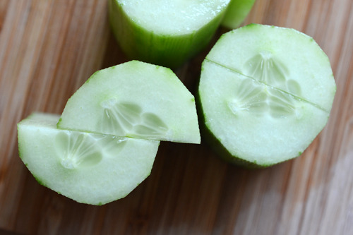 A cucumber is cut into smaller chunks and cut in half.