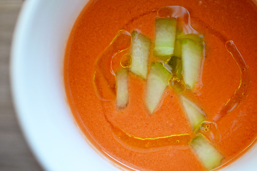 Watermelon and Tomato Gazpacho in a bowl topped with cucumber pieces and olive oil.