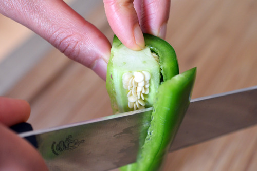 Someone cutting off the flesh of a jalapeño, avoiding the seeds and rib.