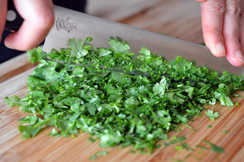 Someone finely chopping up cilantro for spicy pineapple salsa.