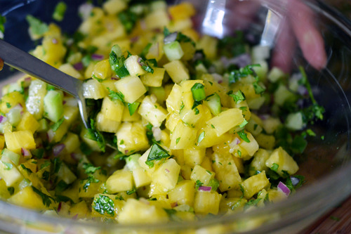 Someone mixing together the ingredients in a bowl for spicy pineapple salsa.