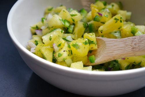 A bowl of spicy pineapple salsa with a wooden spoon.