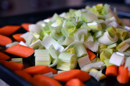 Chopped up leeks and carrots are on a baking sheet.