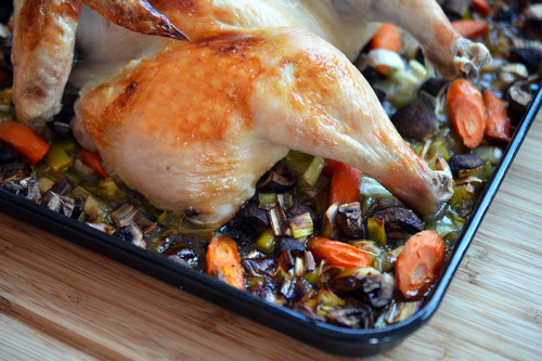 A cooked roast chicken on a pan with veggies underneath.