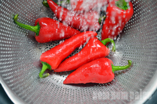 An overhead shot of red jalapeño peppers in a colander as they are being rinsed with water.